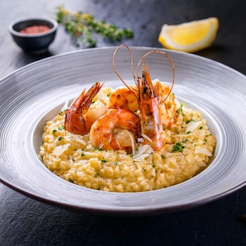 Risotto aux gambas features creamy Arborio rice topped with grilled prawns and garnished with colorful accents for an indulgent experience.