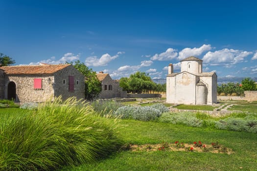 Old, dated on 9th century, Church of the Holy Cross in Nin with grass and flowers in front and mountain range of Dinaric Alps in background, Croatia