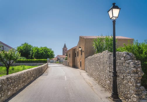 Street with vintage, old buildings, lit street lamp, stone walls and church in background. Old district of Nin town located on small island, Croatia