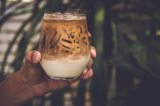 Selective focus Hand Hold Glass of iced coffee on dark summer nature background