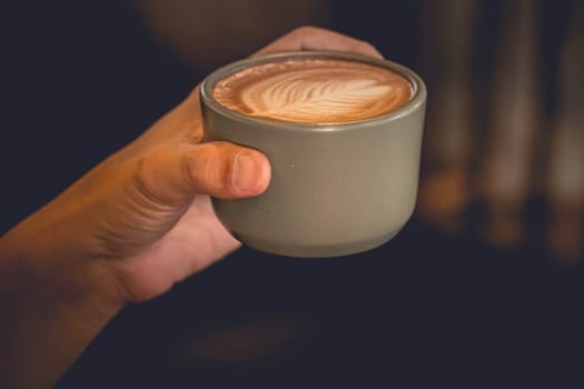 Hand holding a cup of latte coffee top view showing latte art in leaf shape