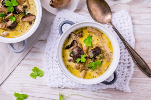 Delicious mushroom soup with herbs in serving pot on wooden table