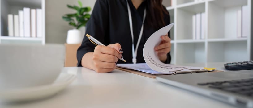 A detail-oriented female financial expert reviews documents while making calculations, showcasing professionalism in a modern office environment.
