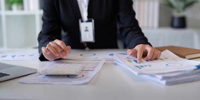 An accountant uses a calculator to compute financial data while reviewing various reports on a desk.