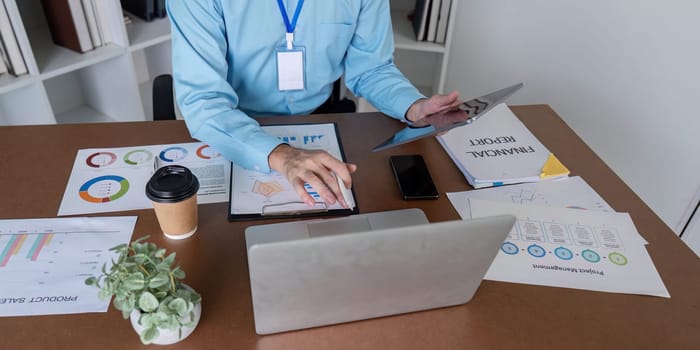 An accountant utilizes a tablet and reviews financial reports while seated at a desk with documents and a laptop.