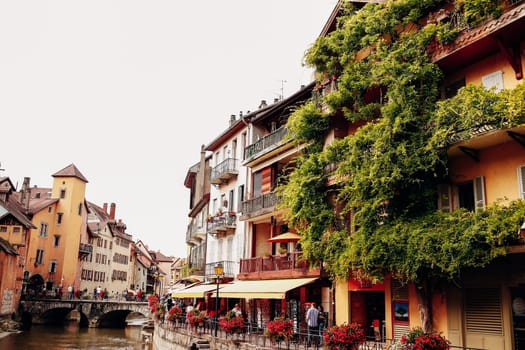 Annecy city water channel, red flowers, old buildings, bridge, green balconies. High quality photo