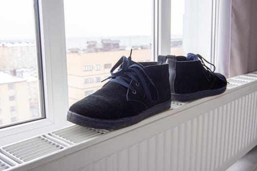 Suede winter boots are dried on a radiator near the window