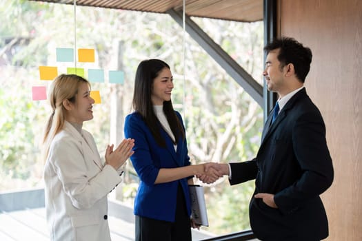 A diverse business team celebrates a successful partnership with a handshake in a bright, contemporary office setting.