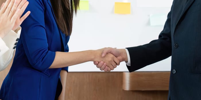 Two diverse colleagues shake hands in a business meeting, representing partnership and mutual agreement in a professional setting.