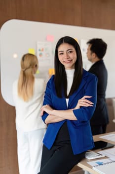 A confident businesswoman stands in front of her diverse team, showcasing leadership and collaboration in a contemporary office space.