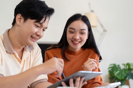 A joyful couple smiles while discussing their finances and budgeting, using a tablet to manage their expenses.
