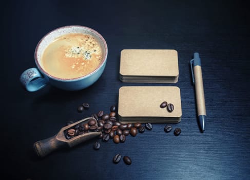Photo of blank kraft business cards, coffee cup, coffee beans and pen on black wooden background. Responsive design mockup.