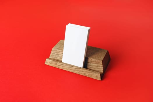 Wooden holder with blank business cards on red paper background.