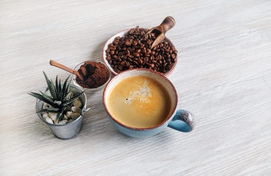 Delicious fresh coffee. Coffee cup, roasted coffee beans, plant and ground powder on light wooden background.