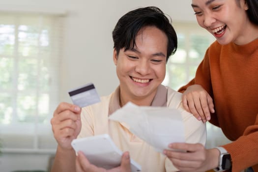 A joyful couple smiles while reviewing their financial documents and credit card, enjoying their budgeting process.