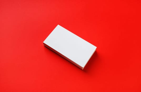 Photo of blank business card on red paper background. Mock-up for branding identity.