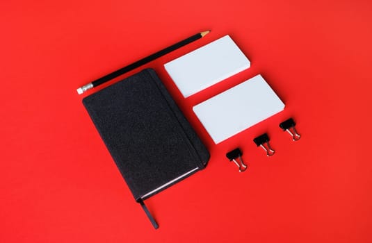Blank notebook, business cards and pencil on red paper background.