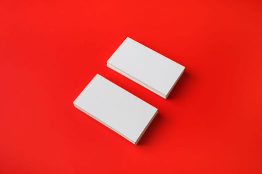 Two blank business cards on red paper background. Branding mockup.