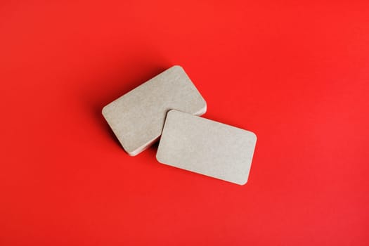 Photo of blank kraft business cards on red paper background. Mockup for branding identity. Blank corporate identity template.
