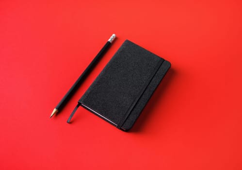 Blank black notebook and pencil on red paper background.