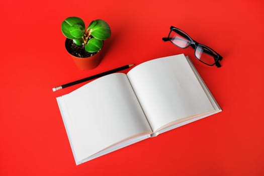 Blank book, glasses, plant and pencil on red paper background. Stationery elements. Template for placing your design.