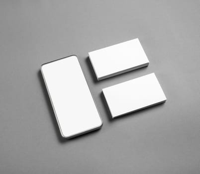 Smartphone and blank business cards on gray paper background. Branding mock up.