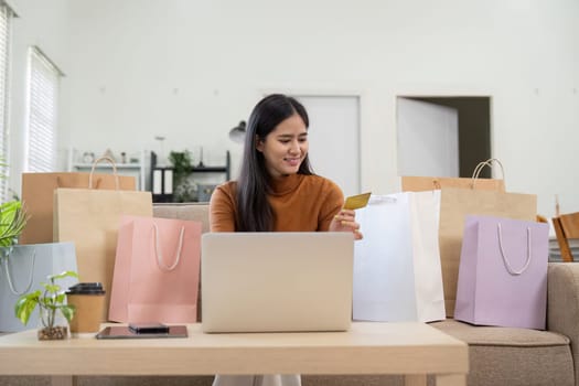 A joyful woman shops online with her credit card, surrounded by shopping bags, expressing excitement over her purchase.