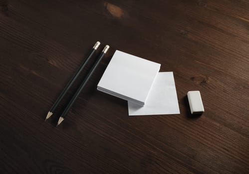 White square notes, pencils and eraser on wooden background. Blank stationery template.