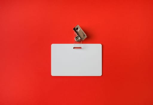 Photo of blank white plastic badge on red paper background. Blank id card. Top view. Flat lay.