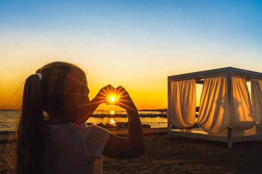 Girl showing with her hands heart, love symbol witch trough shines Sunstar with sunrays, at beautiful sunset on beach at Adriatic Sea, Zaton, Croatia