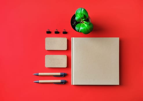 Blank kraft stationery. Book, business cards, pens and plant on red paper background. Top view. Flat lay.