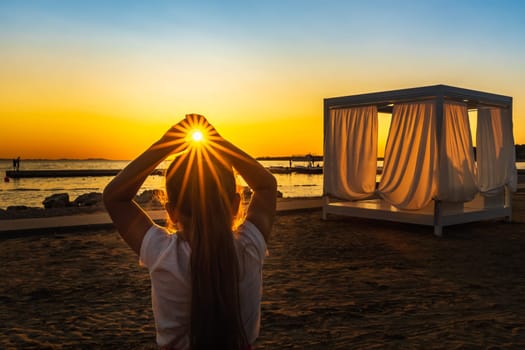 Young girl holding sun in her hands witch trough shines Sunstar with sunrays, at beautiful sunset on beach at Adriatic Sea, Zaton, Croatia