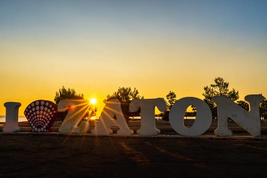 Amazing sunset and silhouette of I Love Zaton text, a welcome sign on the beach at Adriatic Sea with defined Sunstar between letters, Croatia