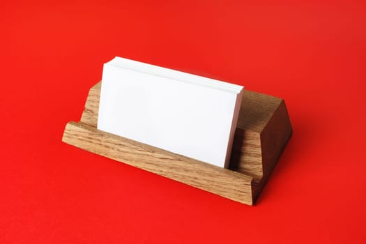 Blank business cards on wooden holder at red paper background. Responsive design mockup.