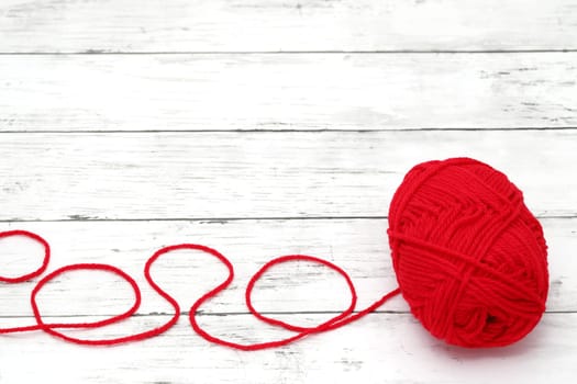 Red ball of wool yarn on a white wooden table