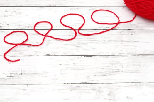 Red ball of wool yarn on a white wooden table