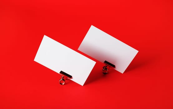Photo of blank business cards and metal binder clips on red paper background.