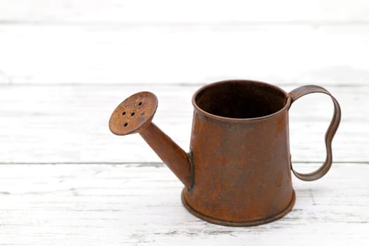 rusted old miniature watering can on wooden white table