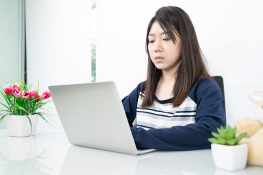 Young female student sitting in living room using laptop at desk learning online