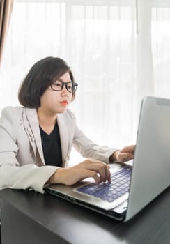 Woman short hair in smart casual wear working on laptop while sitting near window in home office