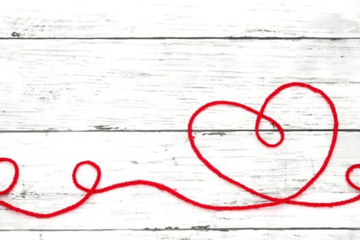 Red woolen thread in the shape of heart on white wooden table　