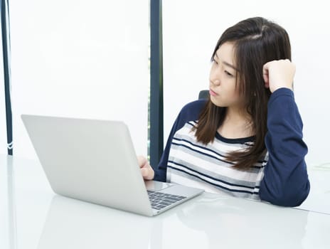 Young female student sitting in living room using laptop at desk learning online