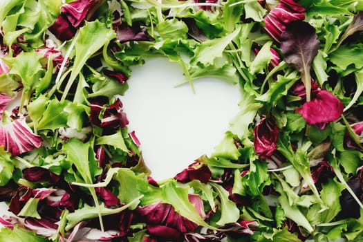 Heart shape from green and purple salad leafs mix background. White table. High quality photo