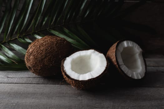 Broken coconuts on gray wooden background with palm leaf. White coconut pulp. High quality photo
