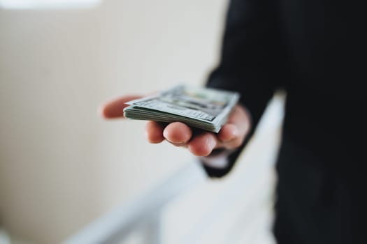 One hundred dollar bills money bundle, in hand of man in suit and white shirt. Blurred background. High quality photo
