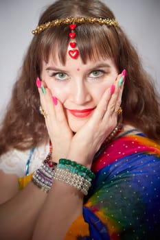 A mature woman poses elegantly in a colorful sari, adorned with traditional jewelry, highlighting her bright makeup and captivating look.