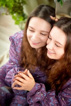 Two women share a joyful moment, embracing each other with smiles while surrounded by warm, inviting decor and soft lighting.