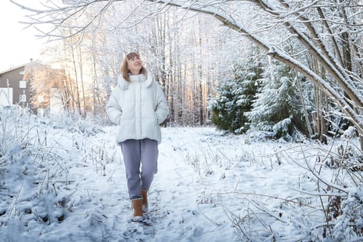 A middle-aged woman strolls through a snow-covered path, enjoying the peaceful winter scenery on a Christmas morning.