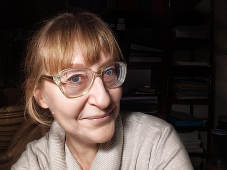 A mature woman with glasses takes a lighthearted selfie at home, capturing a moment of joy and creativity in her blogging journey.