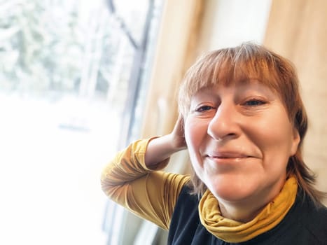 A woman with blonde hair poses happily indoors, embracing the winter vibes while documenting her travel experiences.
